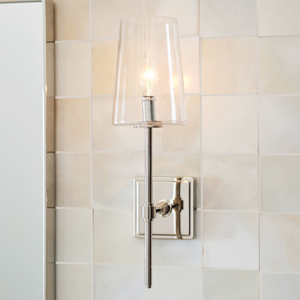 Close view of the clear glass shade, reflective metal arm and wall mounting plate