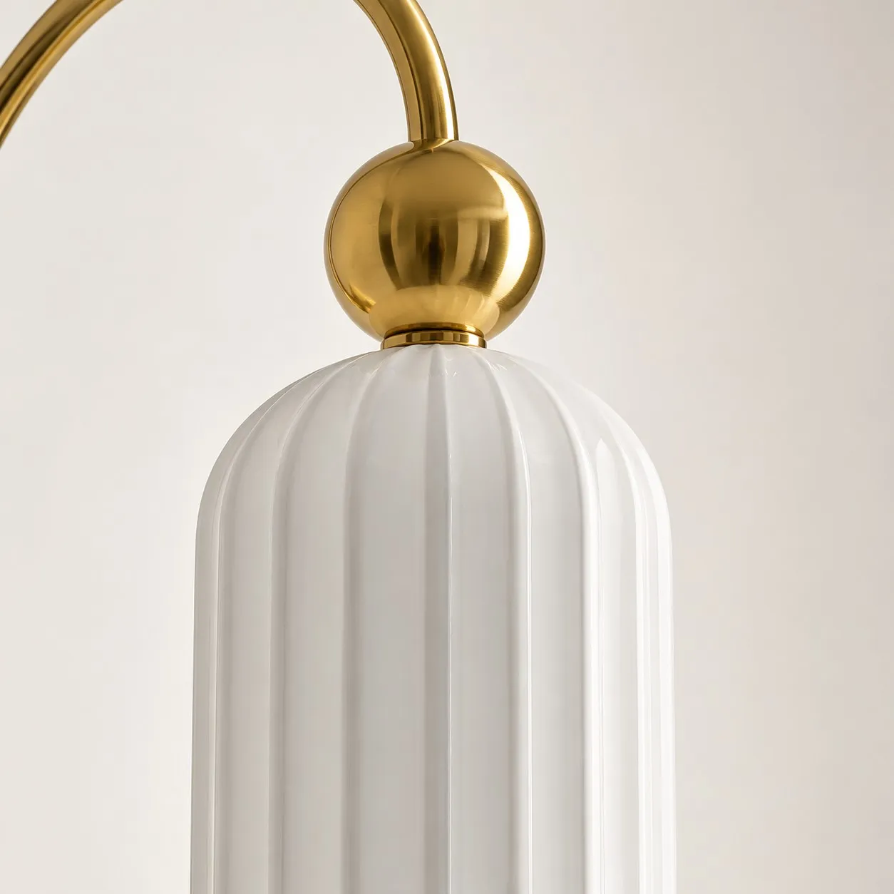 Curved gold-tone arm and spherical detail above a white fluted glass shade